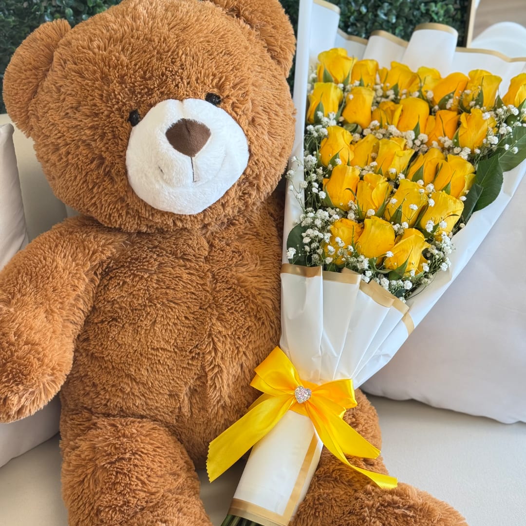 Teddy bear beside a bouquet of yellow roses wrapped in white paper