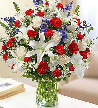 Bouquet of white lilies, red carnations, blue flowers, and white roses in a glass vase