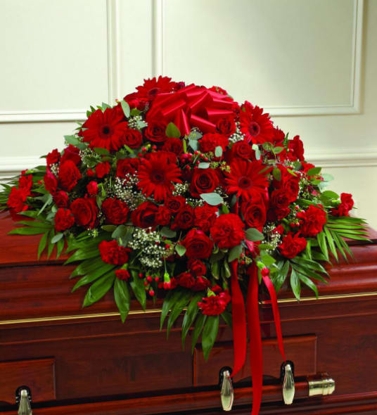 Red floral casket spray with ribbon on a wooden coffin