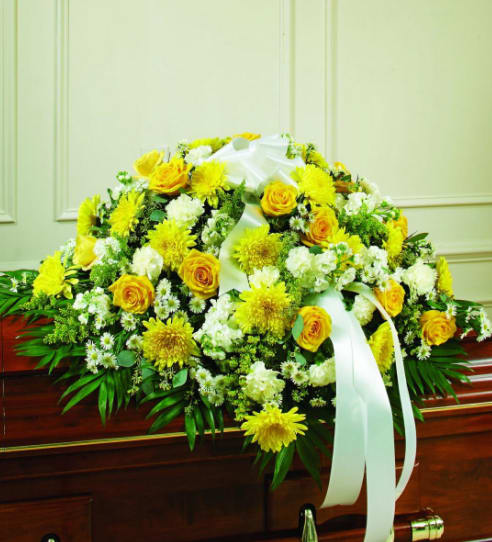 Yellow and white floral casket spray with ribbon on a wooden casket
