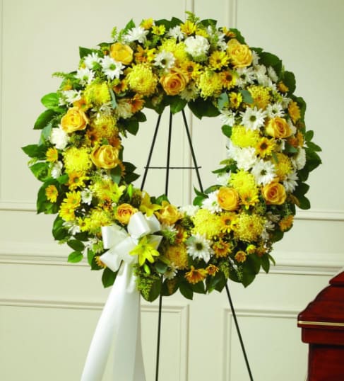 Yellow and white floral wreath on a black easel with a white ribbon