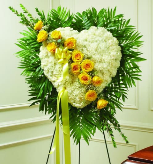 Heart-shaped white floral wreath with yellow roses on a stand