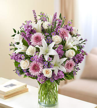 Bouquet of white lilies, pink flowers, and cream roses in a glass vase
