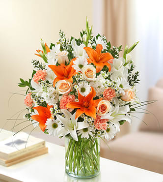 Bouquet of orange lilies, white daisies, and peach roses in a glass vase