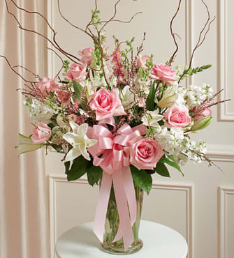 Pink roses and white lilies in a clear glass vase with a pink ribbon