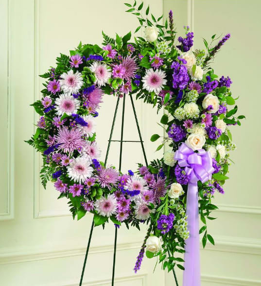 Purple and white floral wreath on a stand with a lavender ribbon