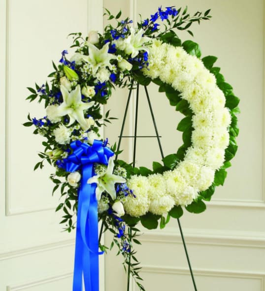 White floral wreath with blue ribbon on a stand