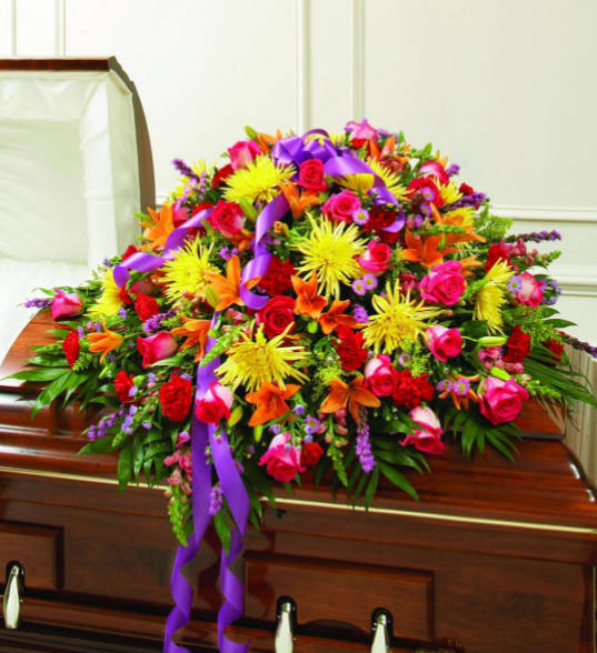 Colorful floral casket spray with purple ribbon on a wooden casket