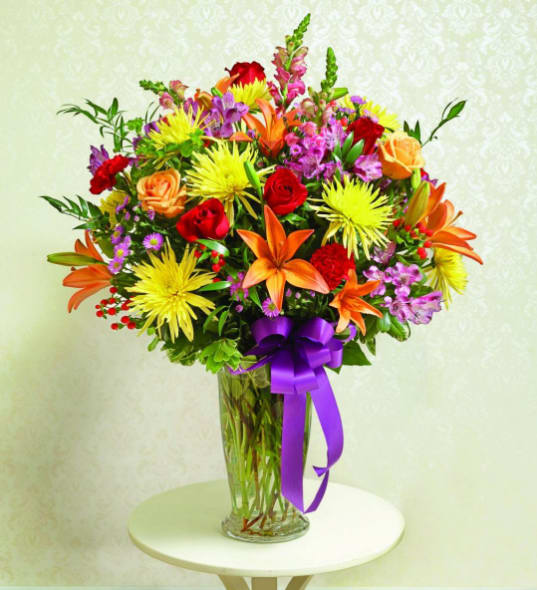 Colorful mixed bouquet in a clear glass vase with a purple ribbon