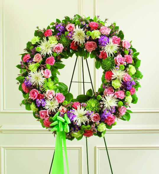 Floral wreath with pink, purple, white, and green blooms on a black stand