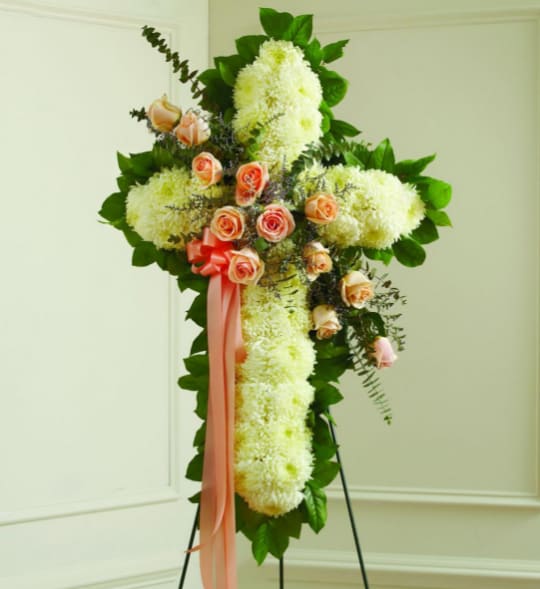 Cross-shaped floral spray with white blooms, peach roses, and a pink ribbon