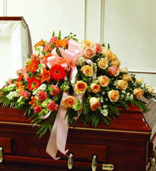 Large floral spray with roses, gerbera daisies, and lilies on a casket
