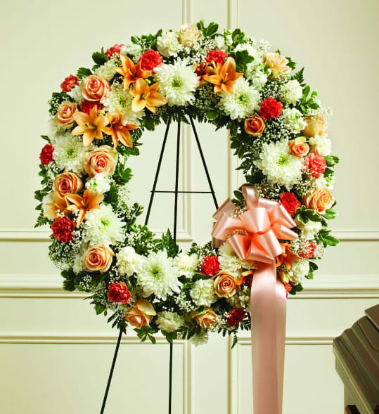 Floral wreath with orange roses, white mums, and a peach ribbon on a stand