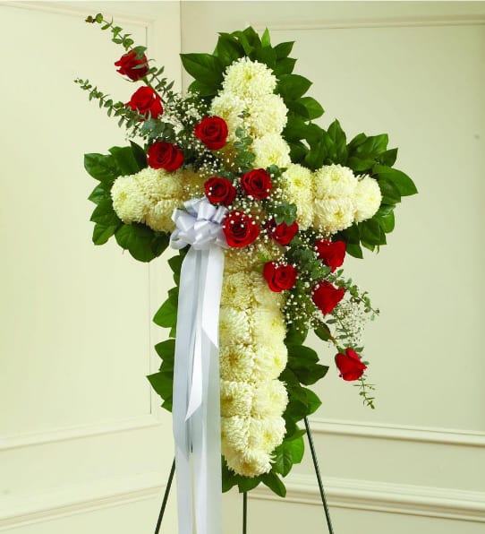 Standing floral cross with white flowers, red roses, and a white ribbon