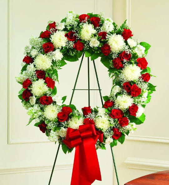 Red and white floral wreath on a stand with a red bow
