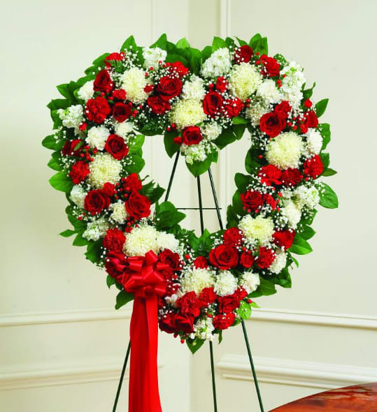 Heart-shaped wreath of red and white flowers on a stand with a red bow