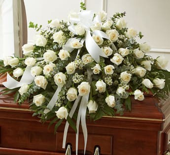 White rose casket spray with white ribbon on a wooden casket