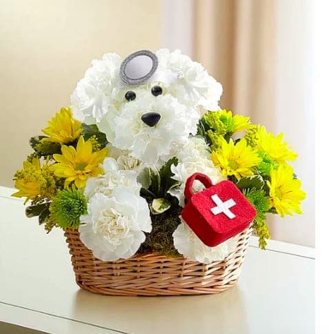 White flower teddy bear in a wicker basket with yellow flowers and a red first-aid bag