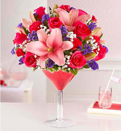 Pink lilies and roses arranged in a tall martini glass vase