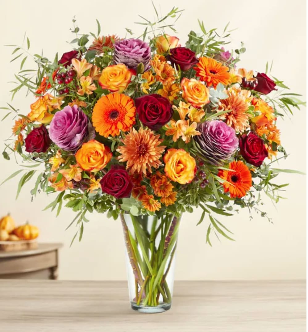 Mixed bouquet of roses, gerbera daisies, and orange blooms in a clear vase