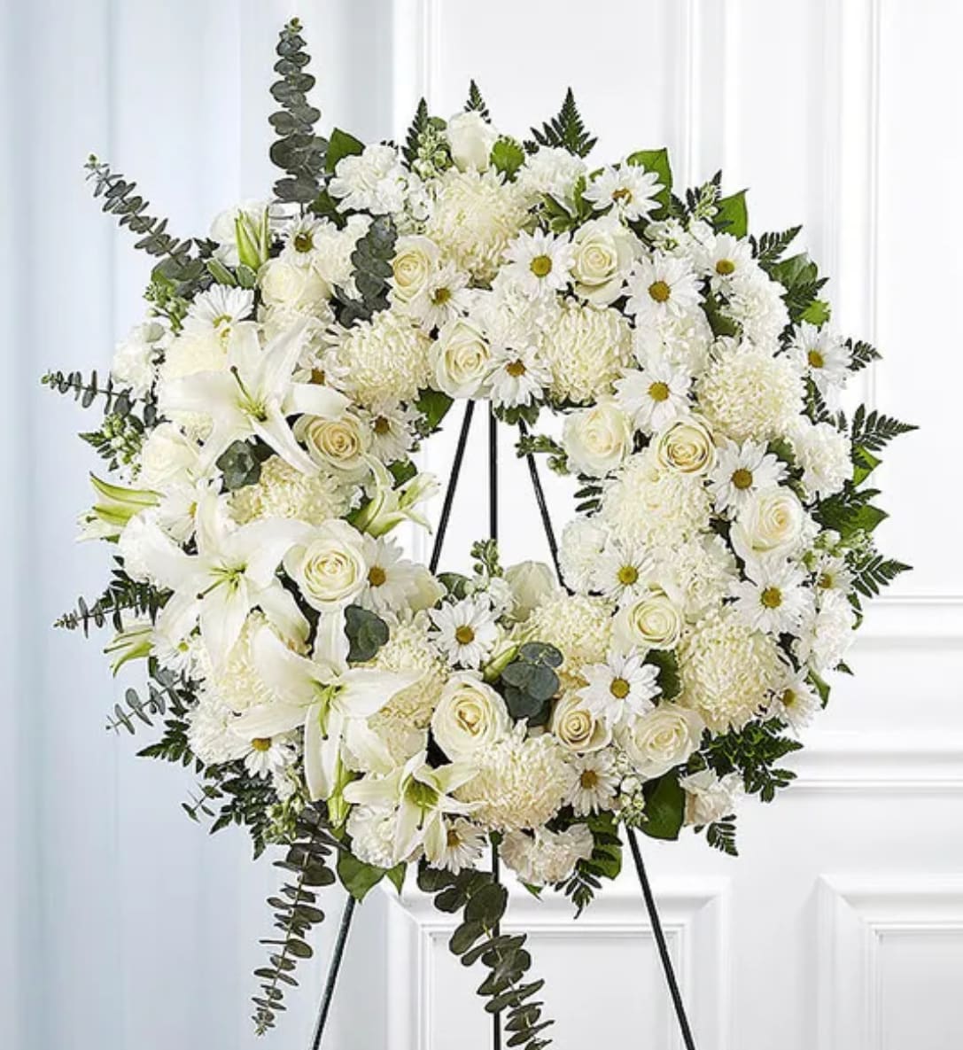 White floral wreath on a black easel with roses and lilies