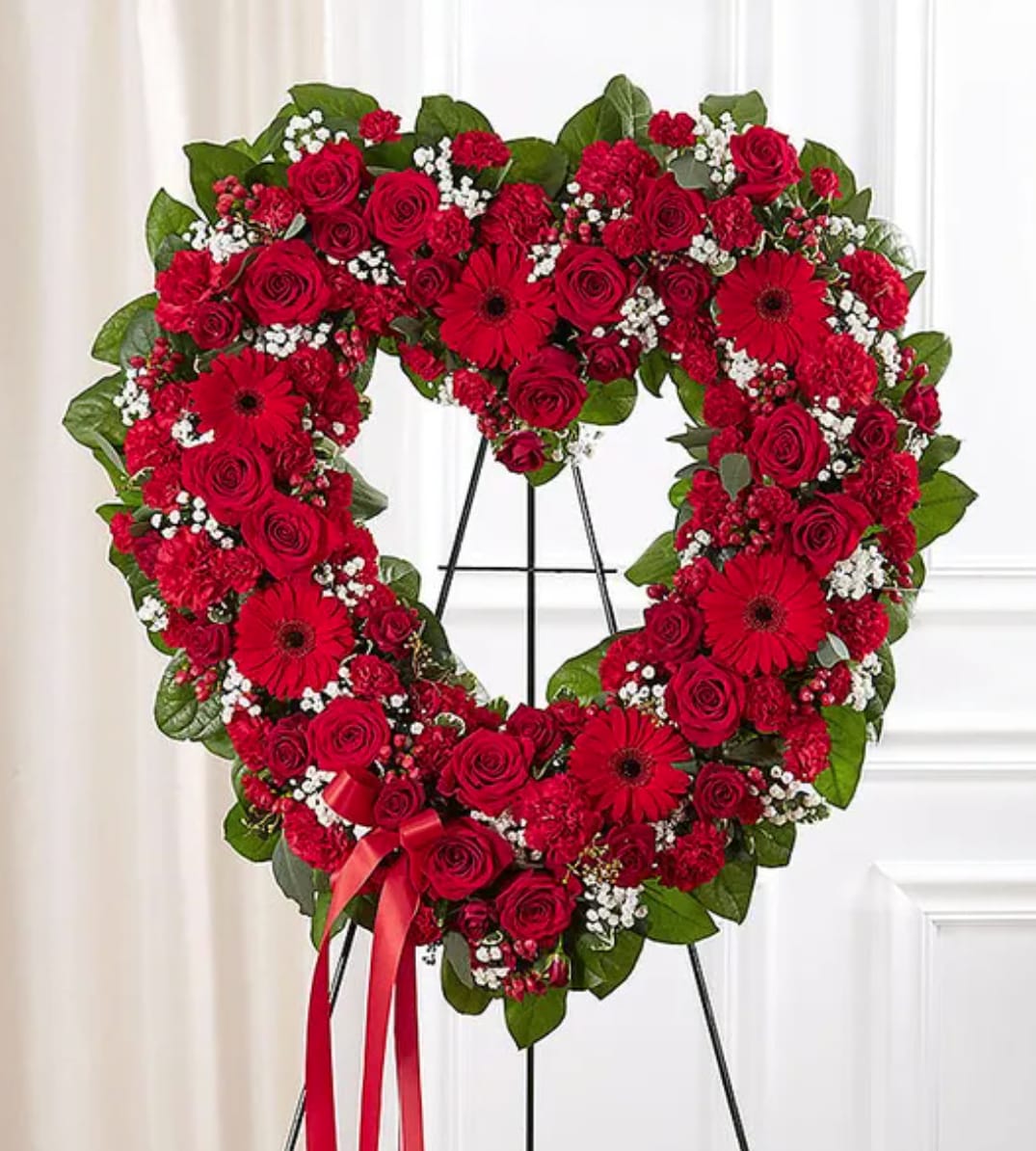 Heart-shaped red floral wreath on a stand with a red ribbon