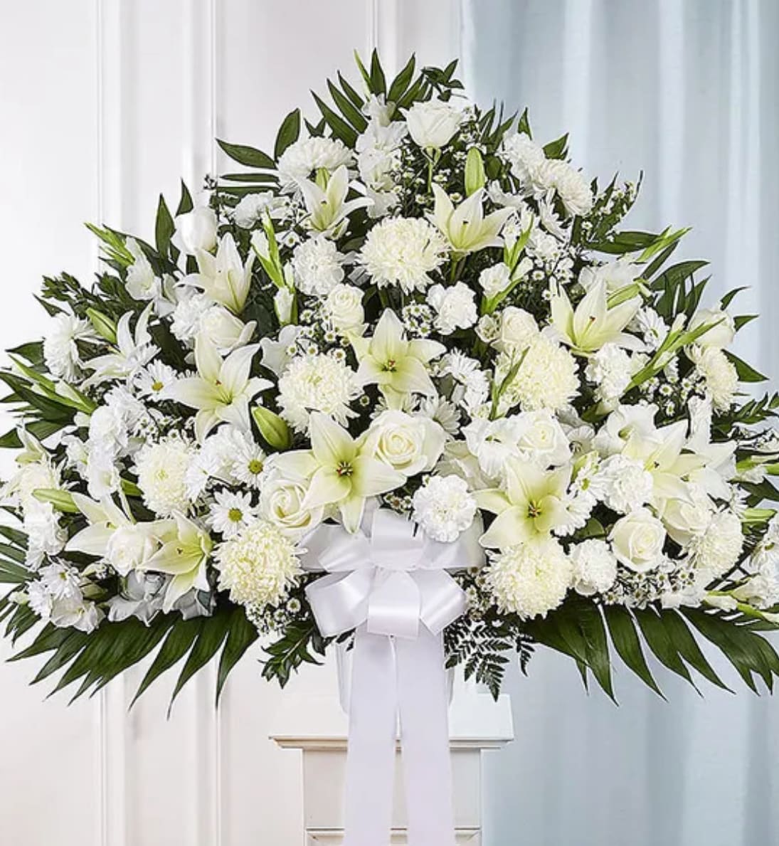 Large white funeral spray with lilies, roses, and chrysanthemums on a stand