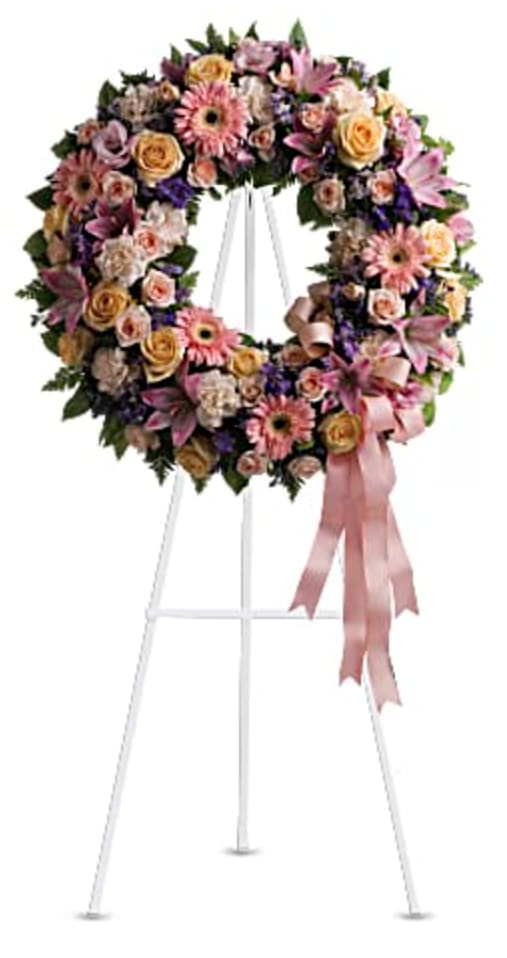 Large floral wreath on a white easel with a pink ribbon