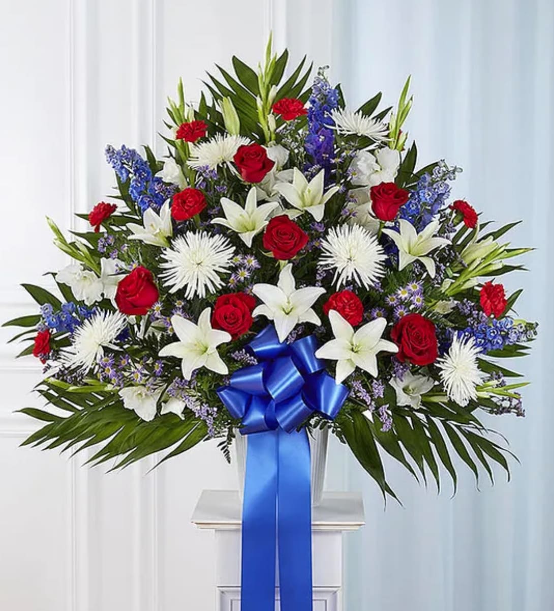 Large standing spray of red, white, and blue flowers with a blue ribbon
