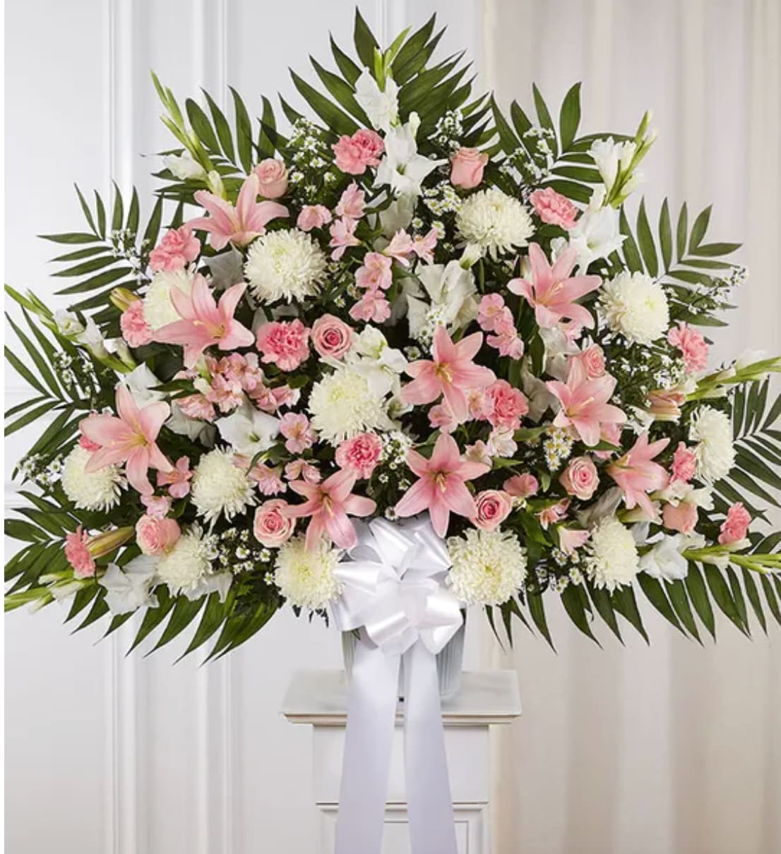 Large pink and white funeral spray with lilies and roses on a stand