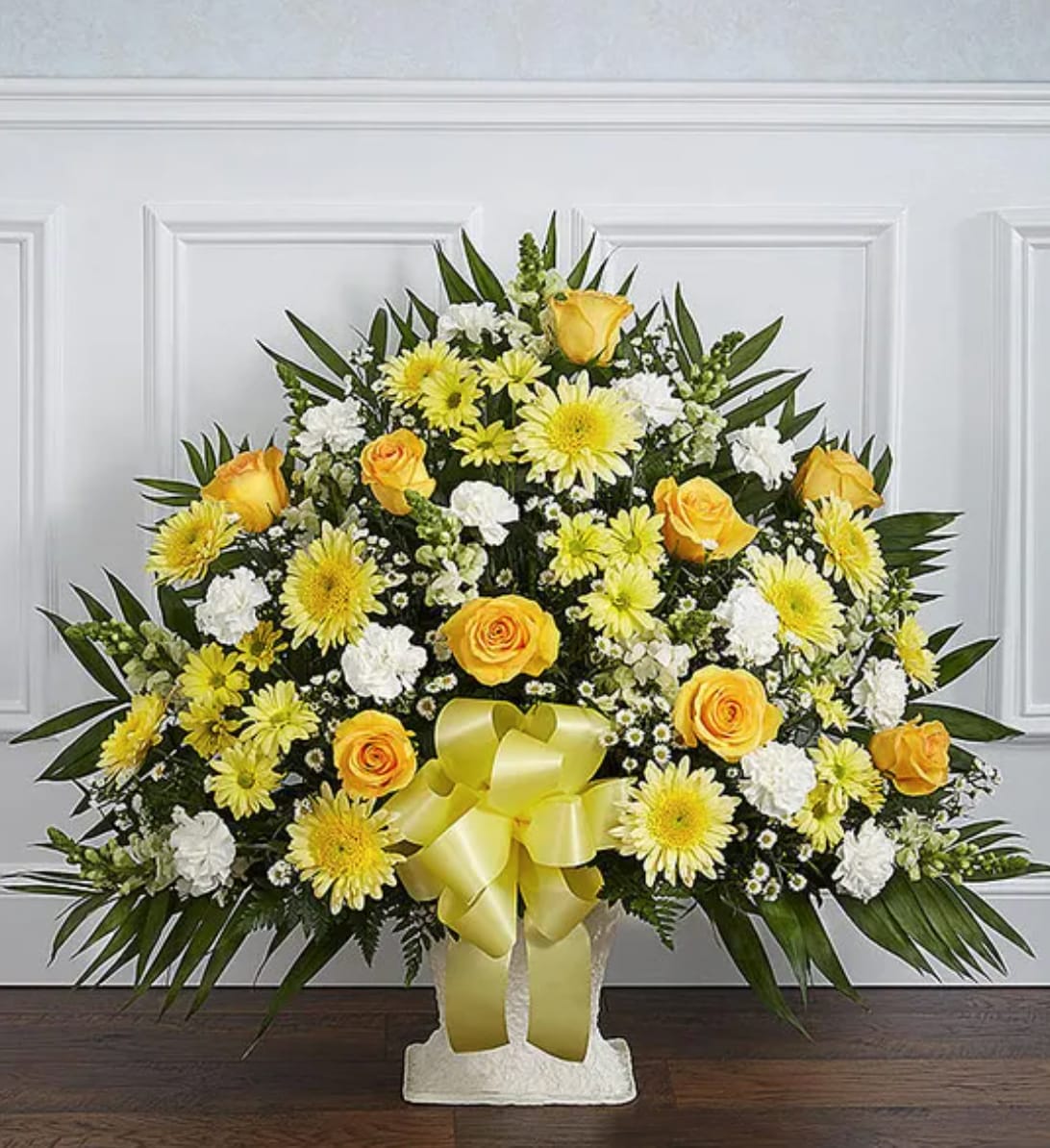 Yellow roses and white daisies arranged in a standing spray with a ribbon bow