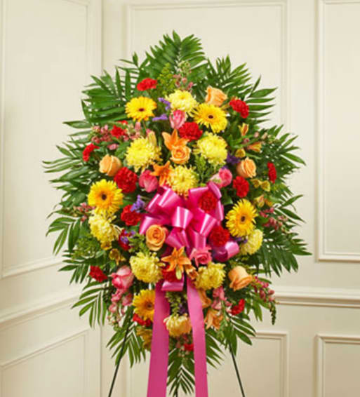 Standing floral spray with mixed bright flowers and a pink ribbon