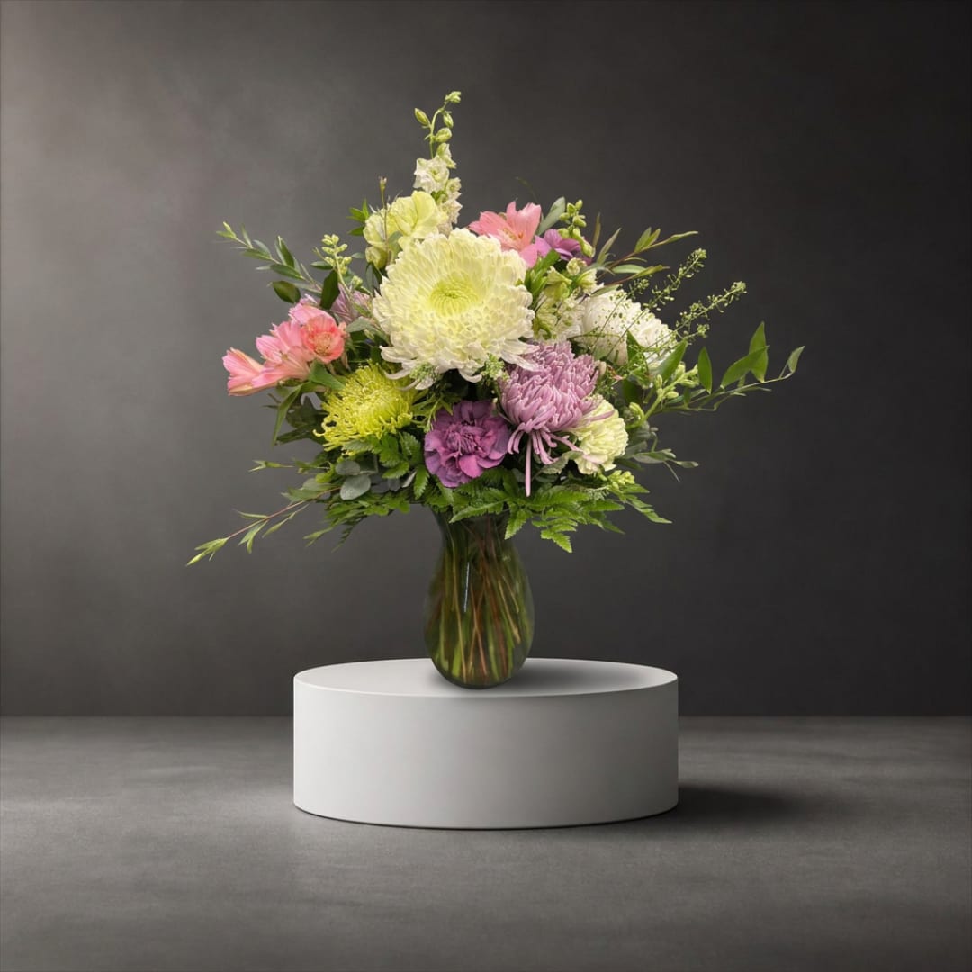 Mixed bouquet of pastel flowers in a glass vase on a pedestal