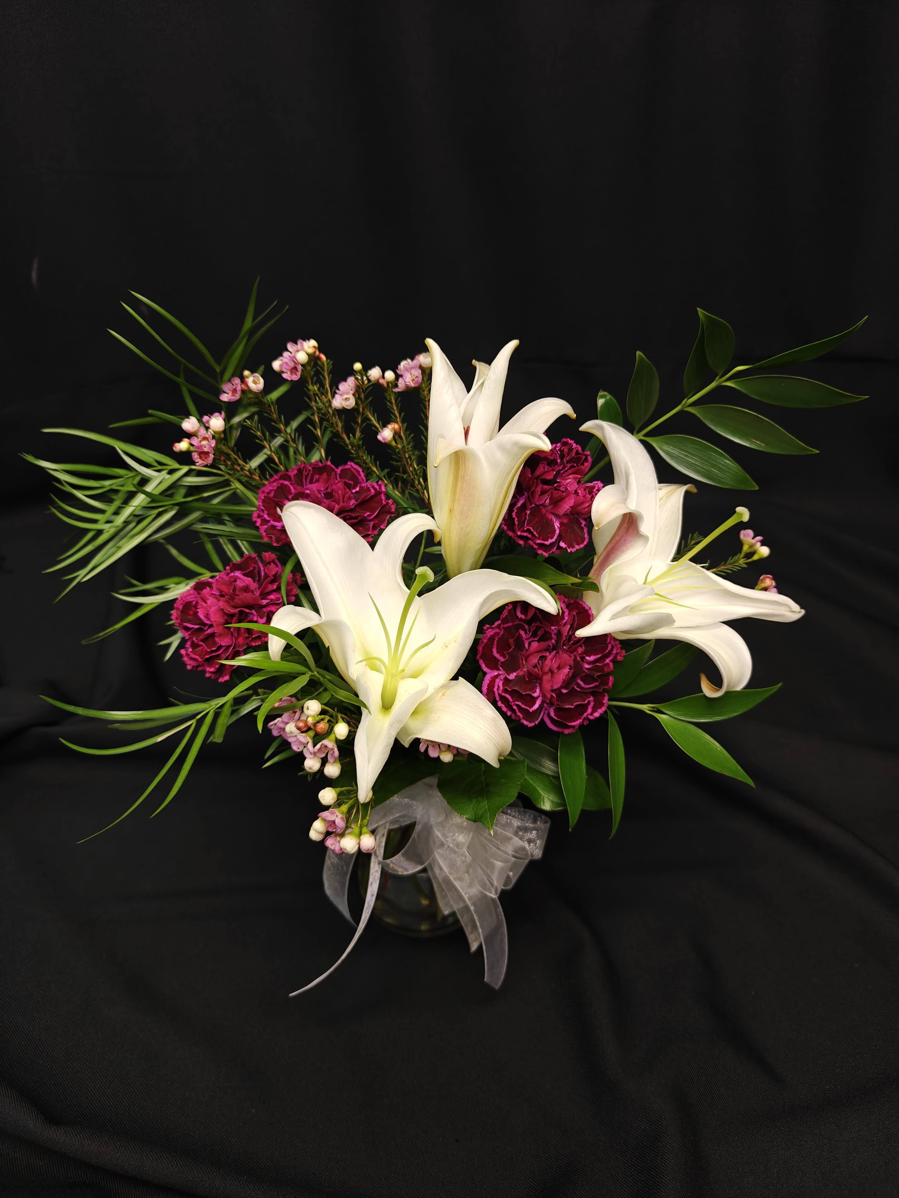 White lilies and magenta carnations in a glass vase with ribbon