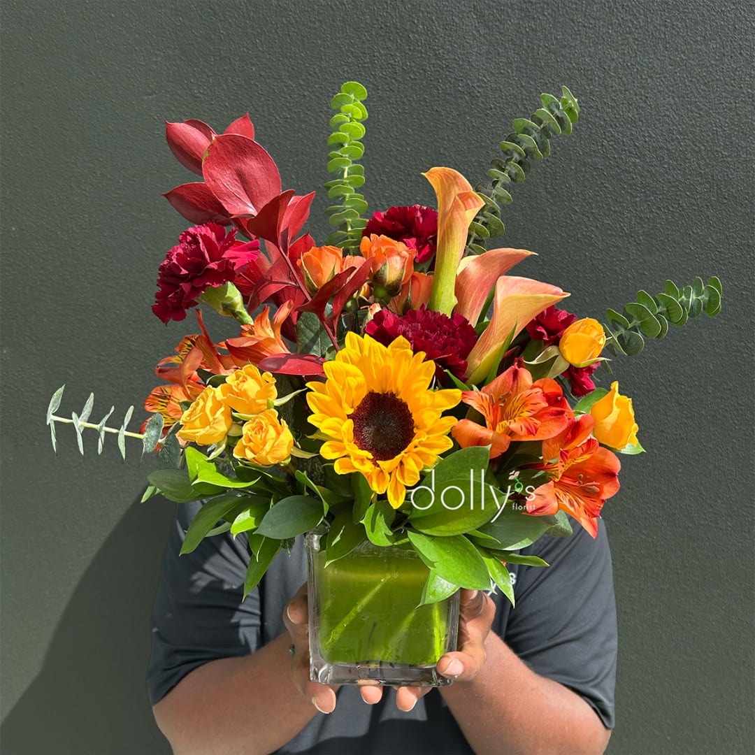 Bright mixed bouquet in a square glass vase with sunflowers, calla lilies, and carnations