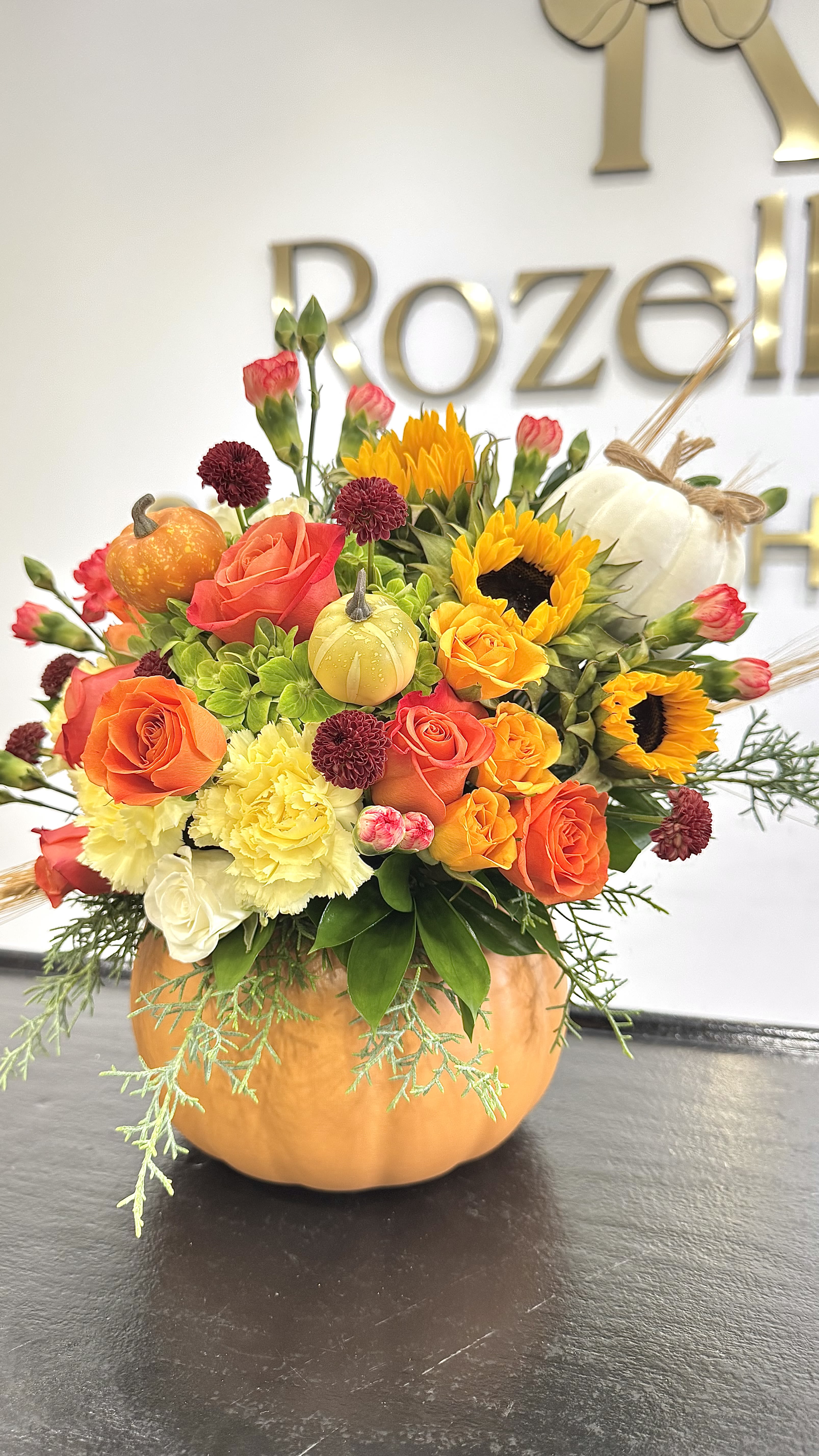 Autumn Pumpkin  - Celebrate the beauty of fall with our handcrafted Autumn Pumpkin Bloom Arrangement. This charming design features a fresh mix of orange roses, bright sunflowers, yellow carnations, and mini gourds, artfully arranged inside a real pumpkin base. Perfect for Thanksgiving tables, seasonal gifts, or cozy home décor, this piece brings warmth, color, and elegance to any space