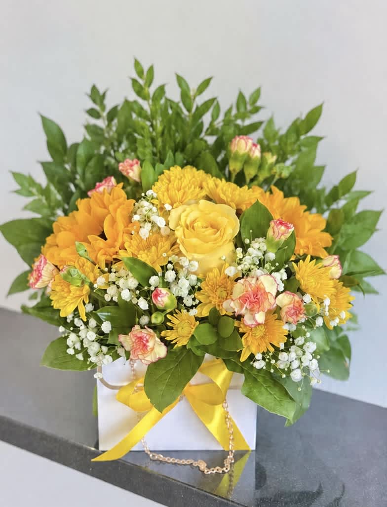 Yellow and orange flower arrangement in a white box with a yellow ribbon