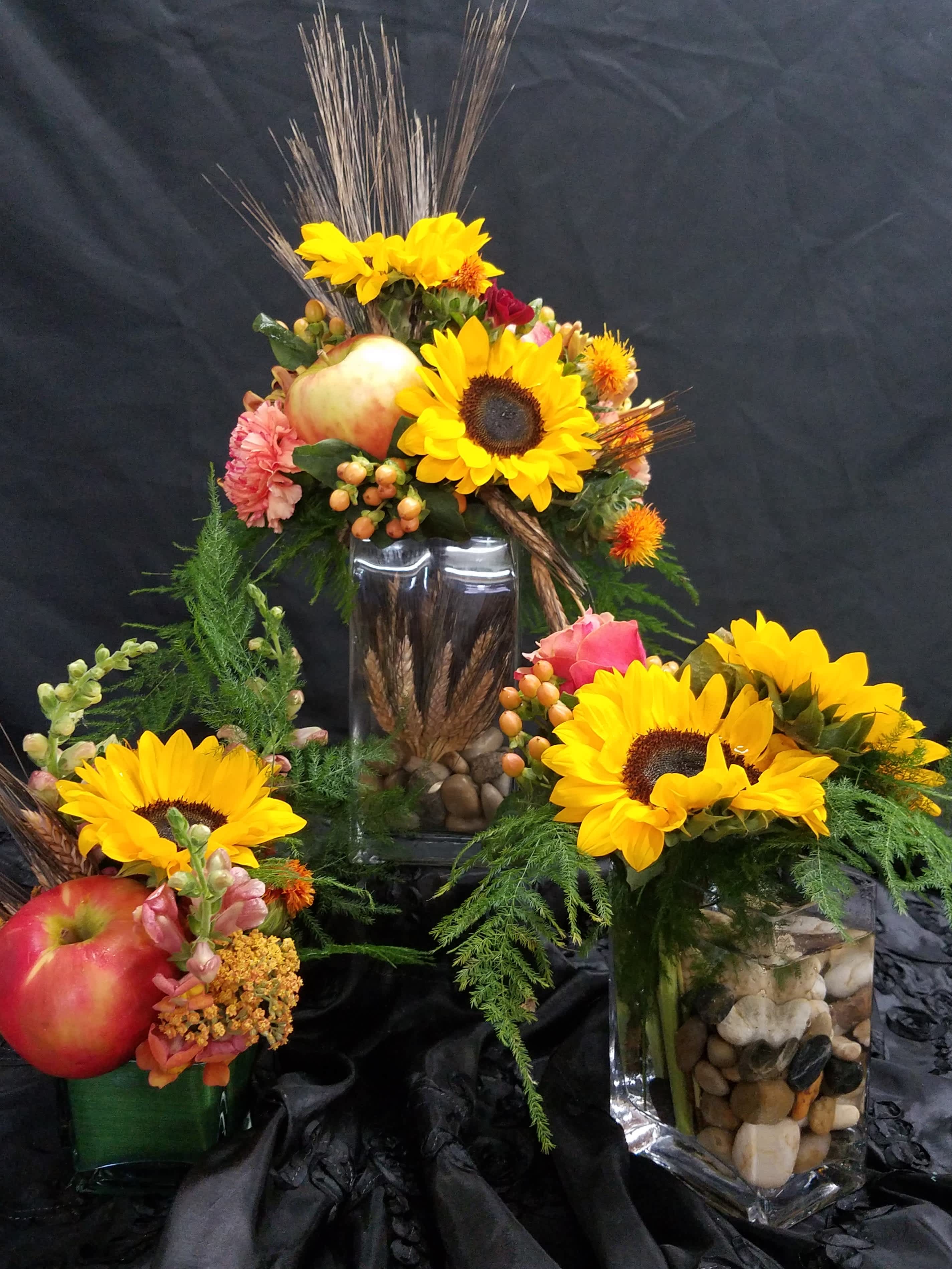 Sunflower arrangements in glass vases with apples and decorative grasses