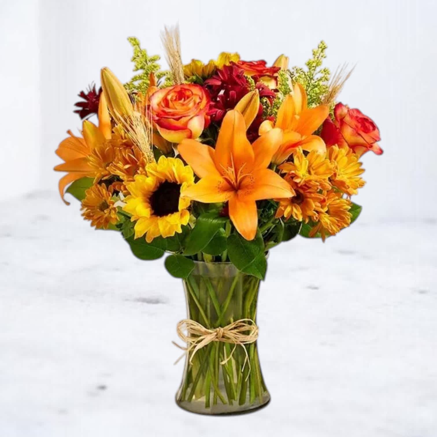 Orange lilies, roses, and sunflowers in a glass vase with a twine bow