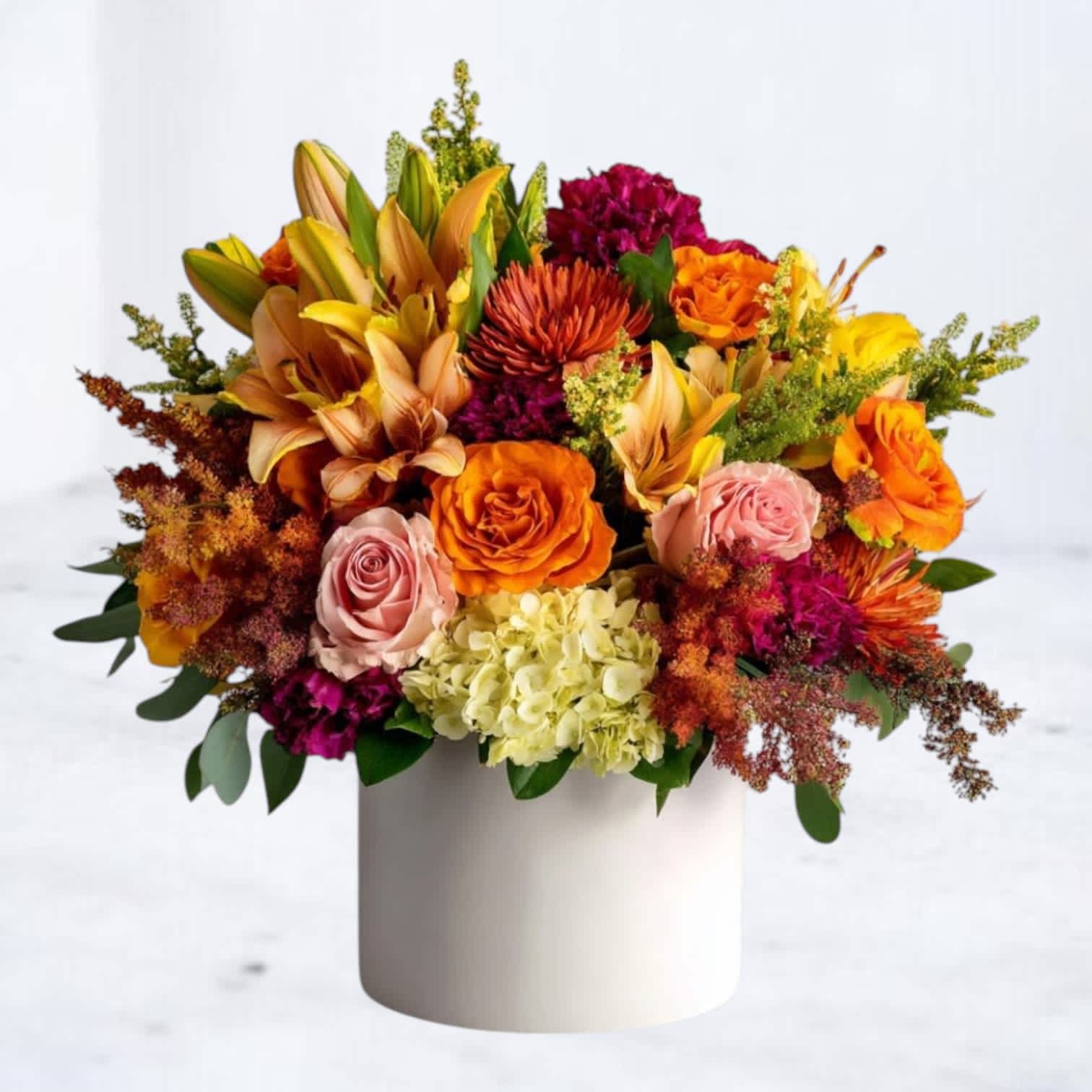 Mixed bouquet of orange, pink, and yellow flowers in a white cylinder vase