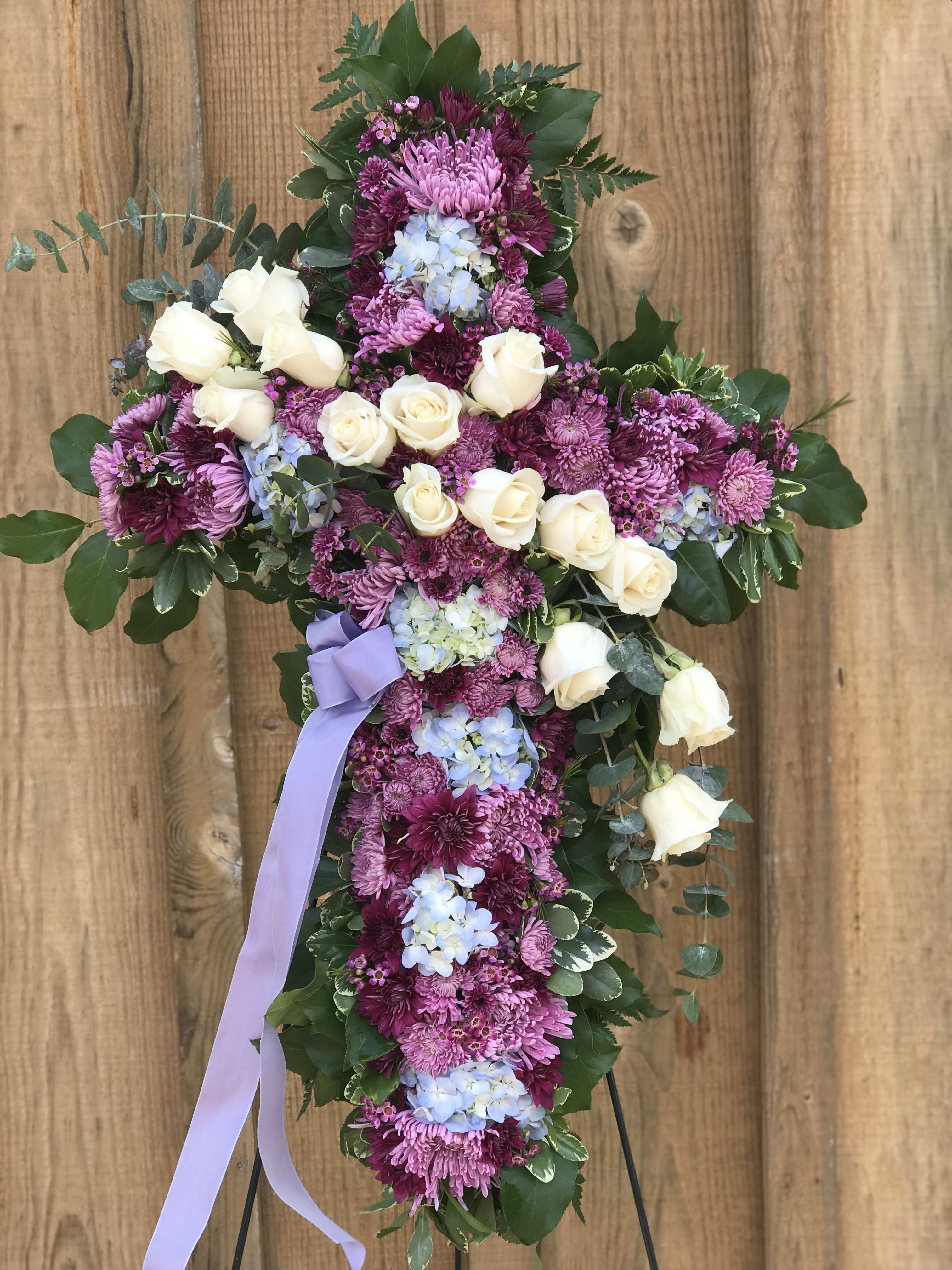 Cross-shaped floral tribute with white roses and purple blooms