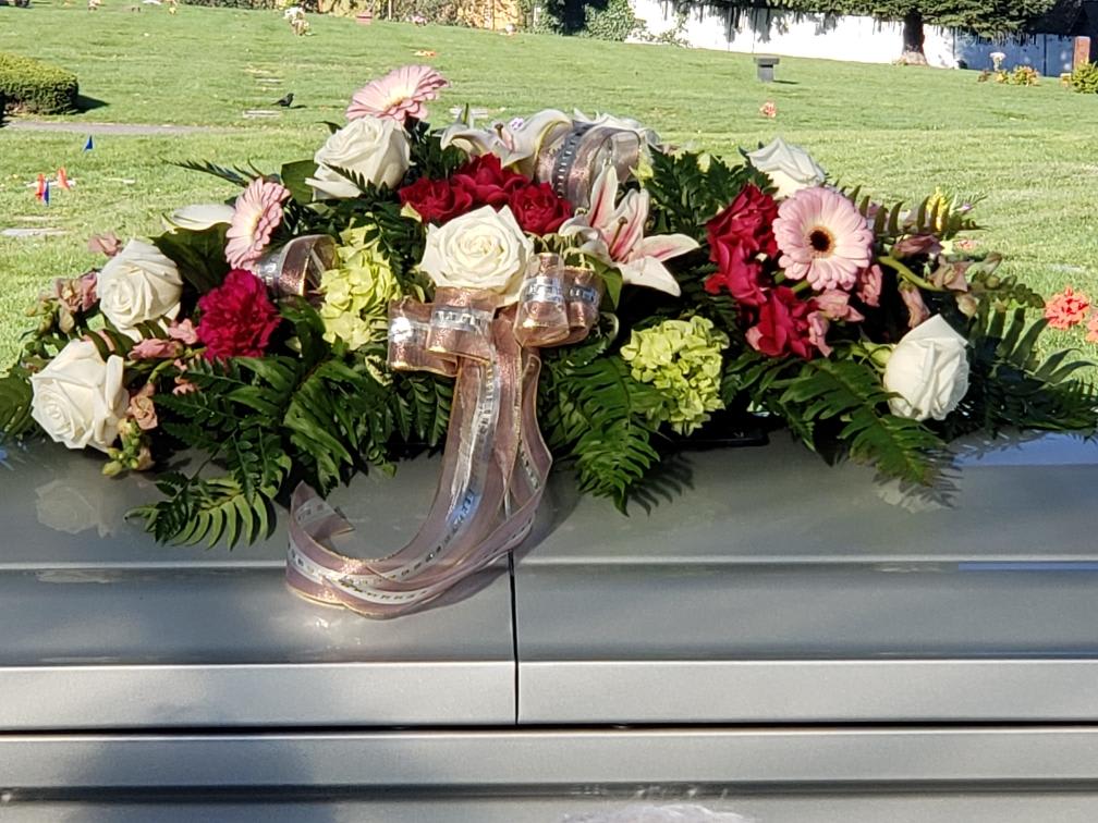 Casket spray with roses, lilies, gerbera daisies, and ribbon