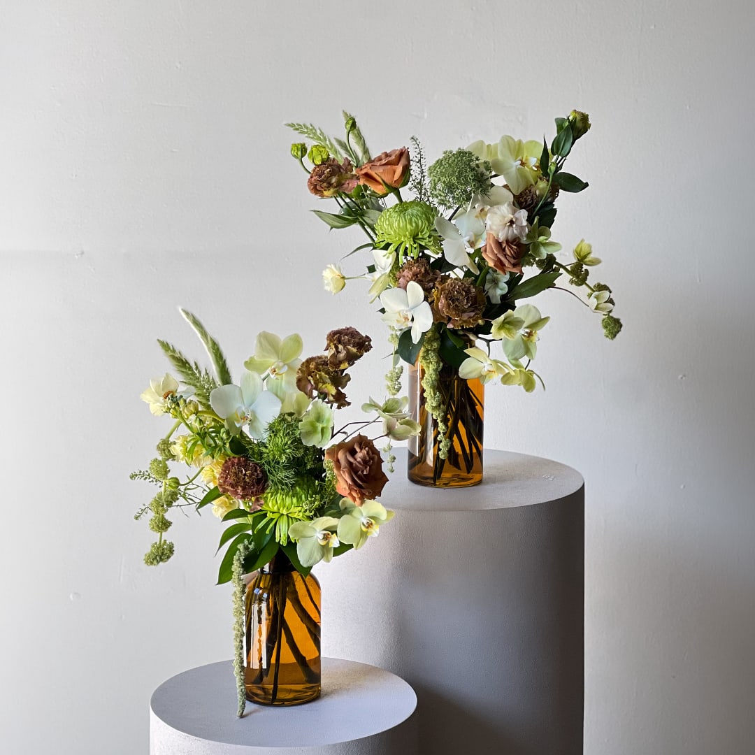 Two floral arrangements in amber glass vases on round pedestals