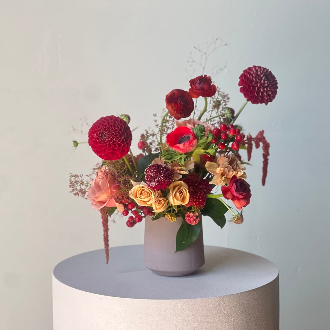 Mixed floral arrangement in a matte vase with red, peach, and burgundy blooms