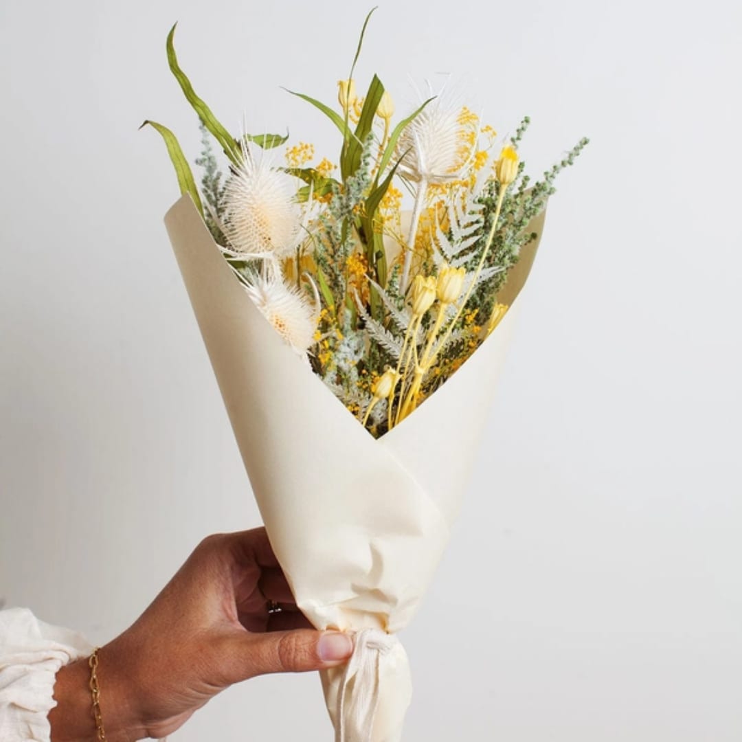 Hand holding a wrapped bouquet with yellow and white dried flowers