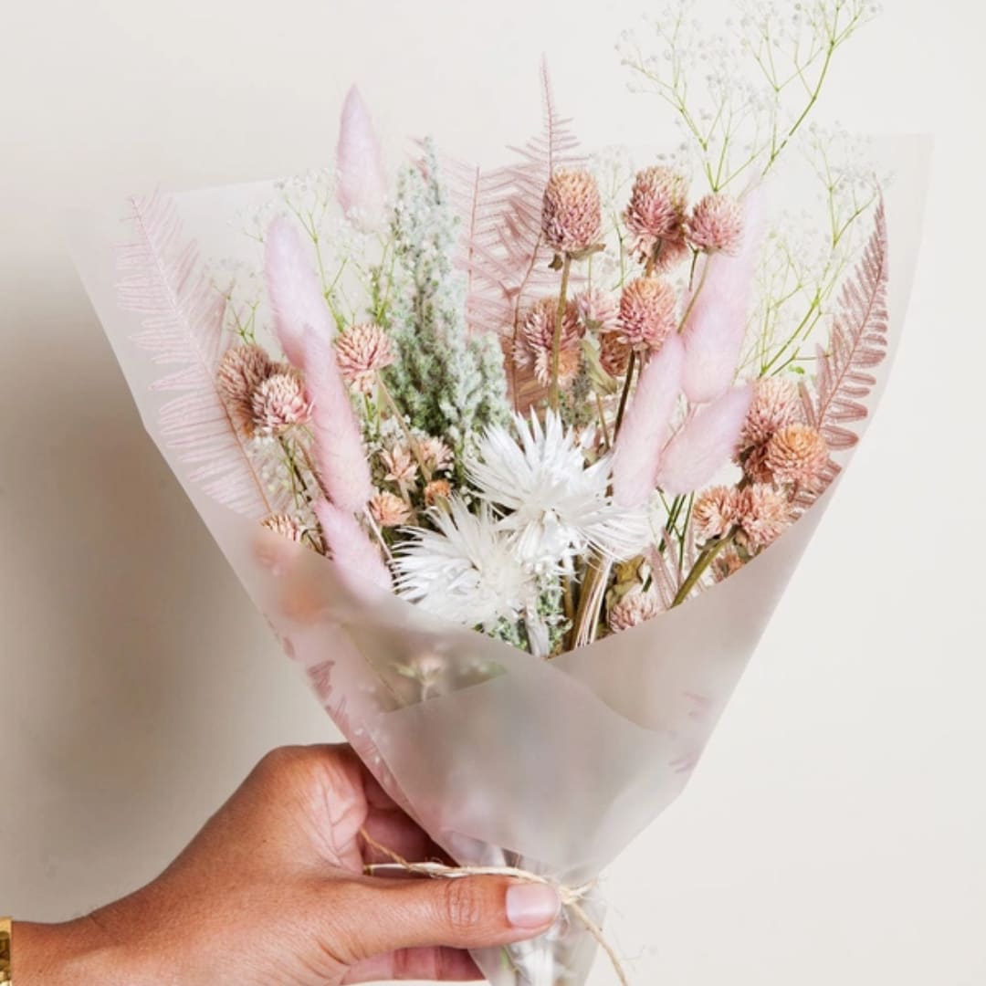 Hand holding a pastel dried flower bouquet wrapped in translucent paper