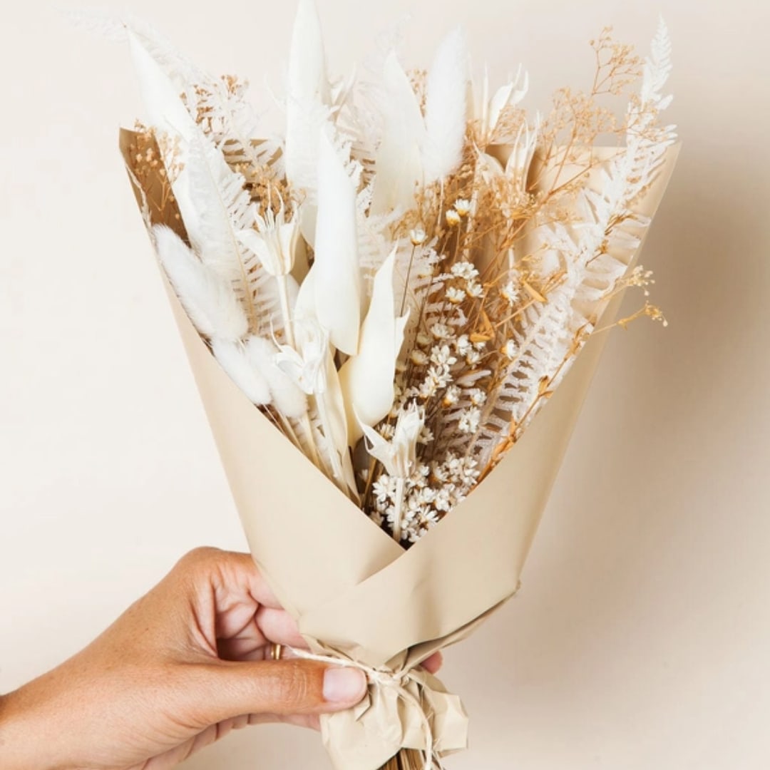 Hand holding a beige-wrapped bouquet of white dried flowers