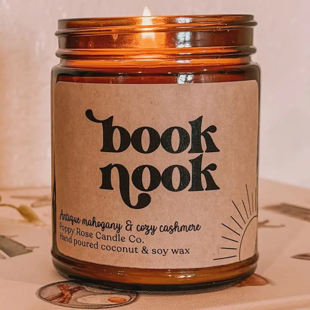 Amber glass candle jar with a lit wick and a paper label reading "book nook"