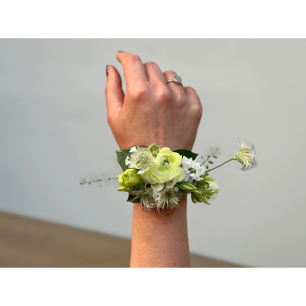 Hand wearing a floral wrist corsage with pale green and white blooms