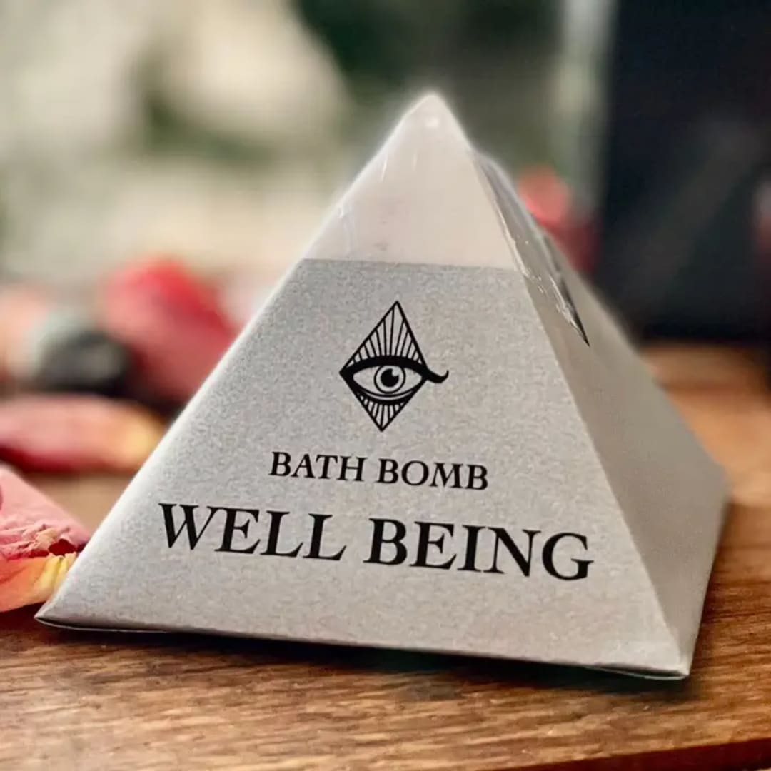 Triangular bath bomb package labeled "WELL BEING" on a wooden surface.